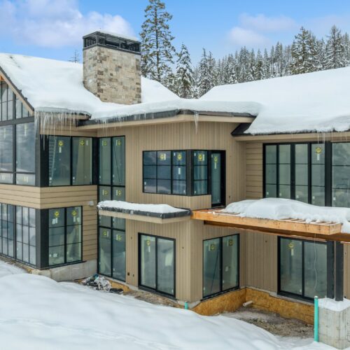 This image depicts a residential building with stunning wood siding and black-framed windows. Snow is covering the ground and the roof.