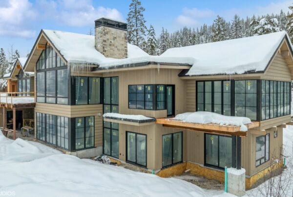 This image depicts a residential building with stunning wood siding and black-framed windows. Snow is covering the ground and the roof.