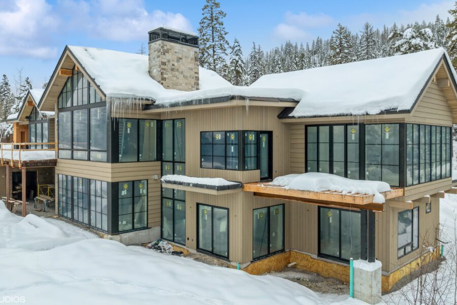 This image depicts a residential building with stunning wood siding and black-framed windows. Snow is covering the ground and the roof.