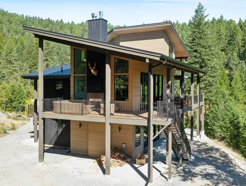 A sleek modern home exterior features rich cedar siding with warm natural tones against a forest backdrop.